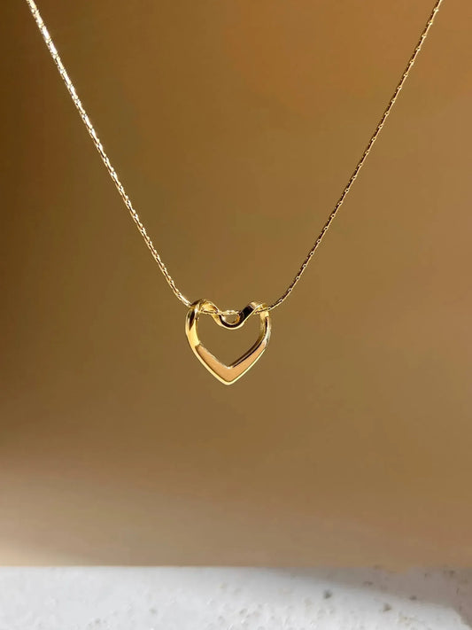 Die vergoldete Edelstahlkette mit Herzanhänger von Cosmos wird vor einem sanften beigefarbenen Hintergrund präsentiert.