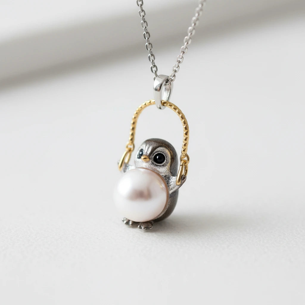 Perlenhalskette "Weise Eule" von flyliving, mit Anhänger eines Pinguins, der eine Perle hält und an einem goldenen Bügel hängt.