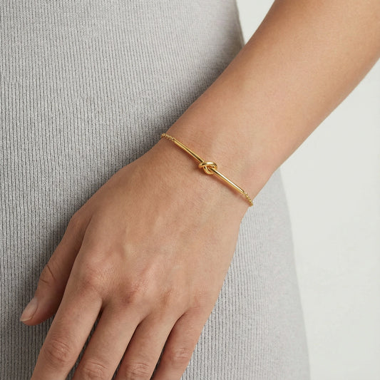 Goldenes Twisted Knot Bar Armband von flyliving, getragen am Handgelenk einer Person.