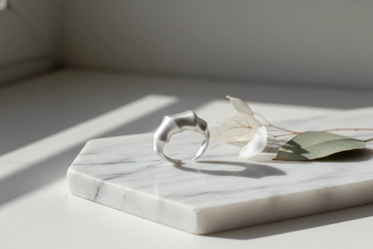 Silberfarbener Statement Ring aus Sterlingsilber von flyliving, auf Marmorplatte mit getrockneten Blumen.