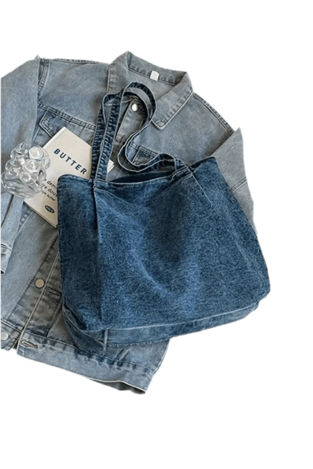 Eine Handtasche „Blue Jeans“, Größe M für Damen, von flyliving liegt auf einer flach hingelegten Jeansjacke, daneben ein Heft mit der Aufschrift „BUTTER“ und ein durchsichtiger Plastikgegenstand.