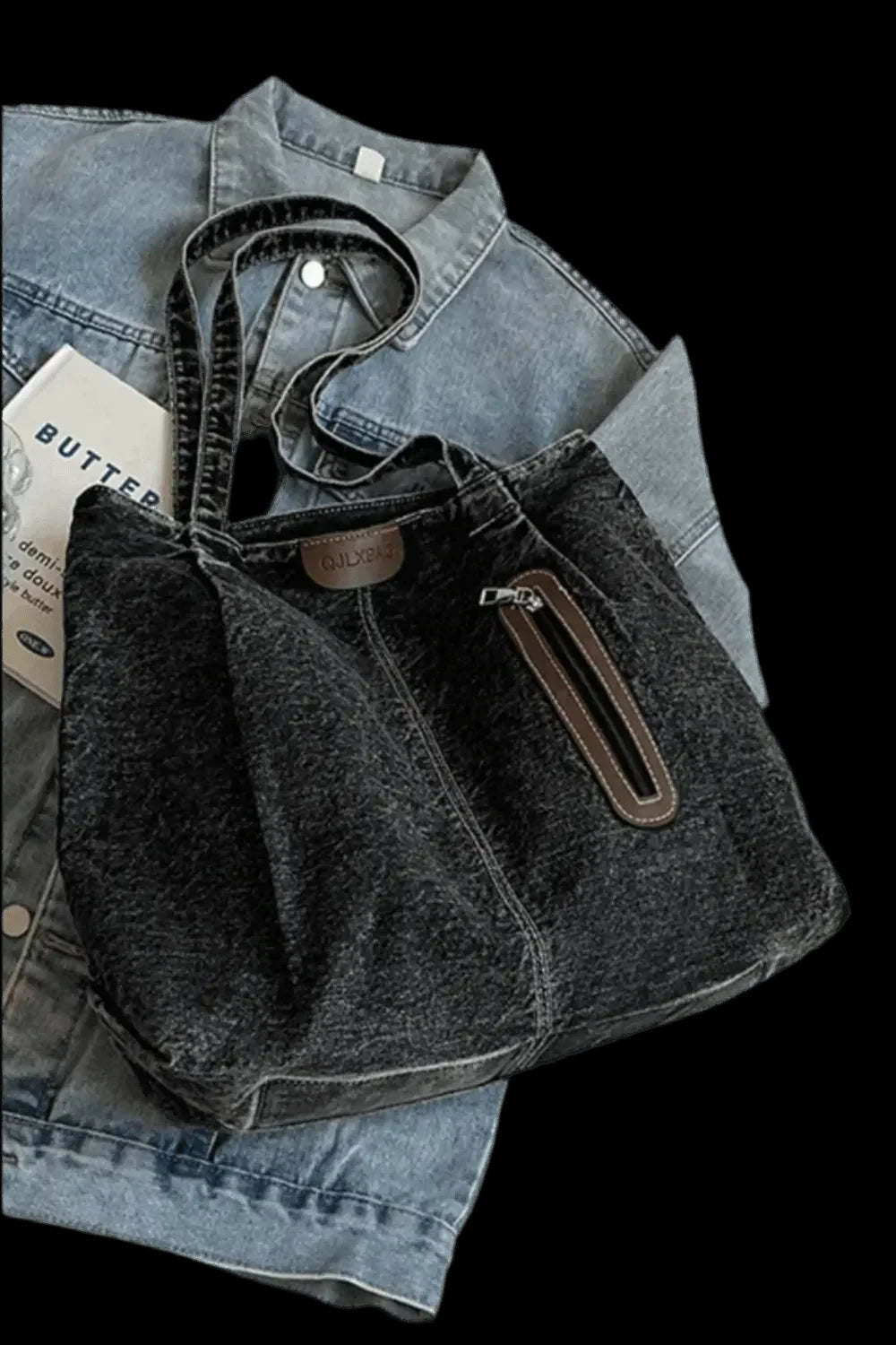 "Die flyliving Handtasche „Blue Jeans“, mittel, für Frauen, in robustem Denim mit Zipper-Tasche, liegt auf einer hellblauen Jeansjacke. Ein Papier mit „BUTTER“ sorgt für einen lässigen Akzent."