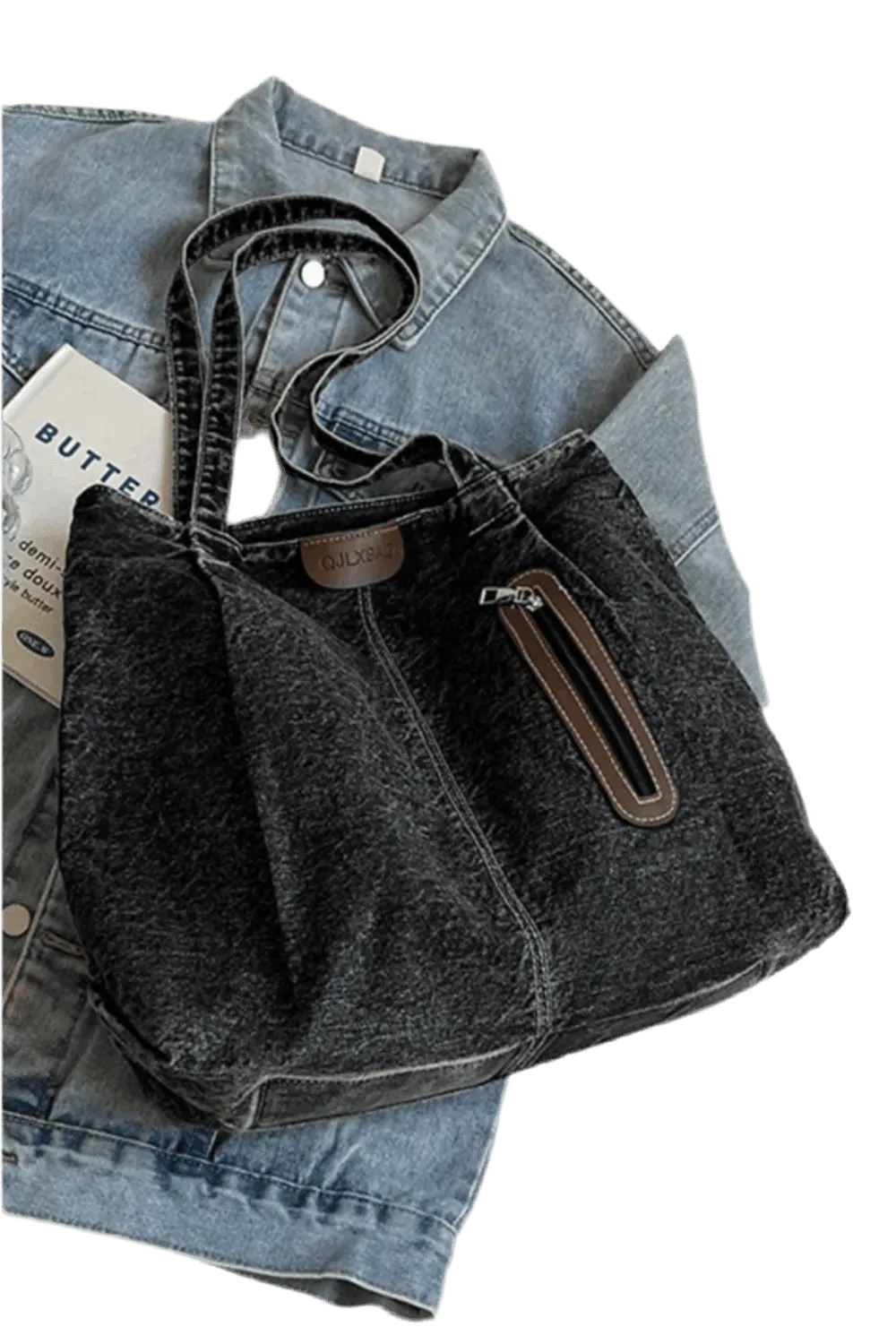 Die flyliving Handtasche „Blue Jeans“, mittel, für Frauen, in robustem Denim mit Zipper-Tasche, liegt auf einer hellblauen Jeansjacke. Ein Papier mit „BUTTER“ sorgt für einen lässigen Akzent.