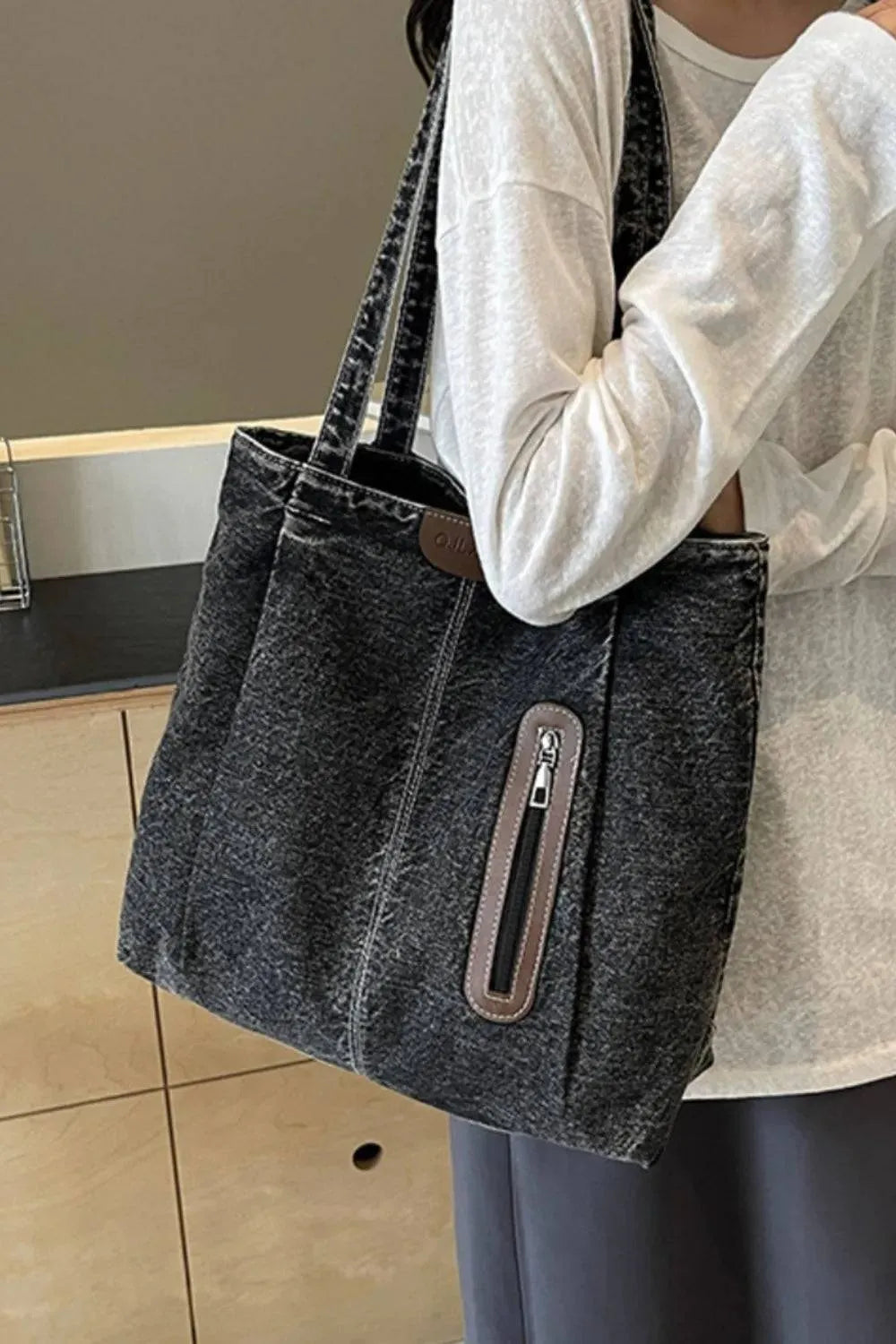 Eine Frau in einem weißen Langarmshirt trägt die mittelgroße Denim-Handtasche „Blue Jeans“ von flyliving mit Fronttasche, Reißverschlussdetail und Markenlogo über der Schulter.
