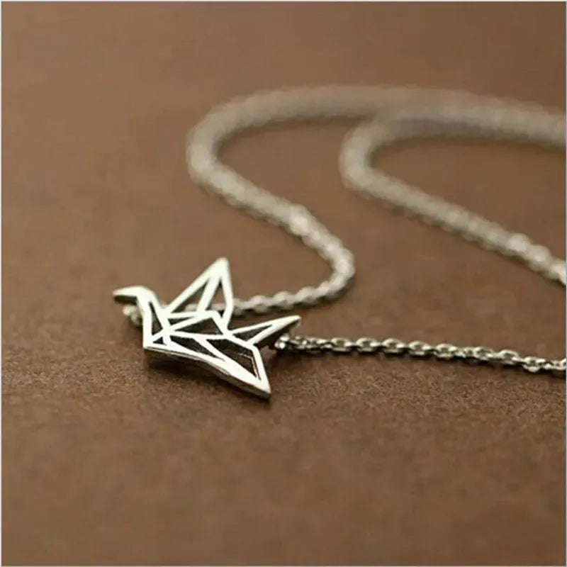 Die Halskette „Wilhelm“ von flyliving – ein filigraner Kranich-Anhänger aus 925er Silber im Origami-Stil – liegt auf einer braunen Fläche.