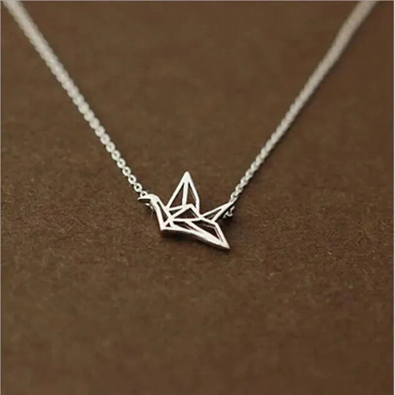 Die Halskette „Wilhelm“ von flyliving ist eine filigrane Silberkette mit Kranich-Anhänger aus 925 Sterling Silber, präsentiert auf braunem Hintergrund.