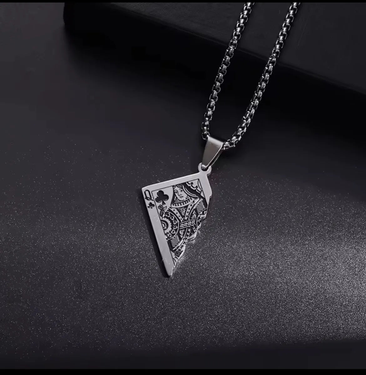Die silberne Halskette „Erna“ von flyliving aus Edelstahl zeigt einen Anhänger in Form einer zerrissenen Spielkarte mit Queen of Clubs Design und wird auf dunkler, strukturierter Oberfläche präsentiert.