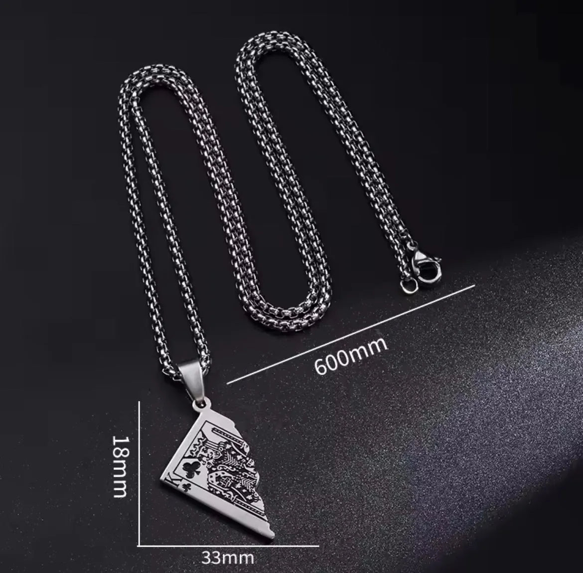 Die Halskette „Erna“ von flyliving in Silber ist eine Halskette aus Edelstahl in Silber mit einer 600 mm langen Kette und einem dreieckigen (33 x 18 mm) Anhänger mit eingravierten Löwen- und Kartenmotiven, inspiriert von Halbspielkarten-Designs, auf Schwarz mit Maßangaben dargestellt.