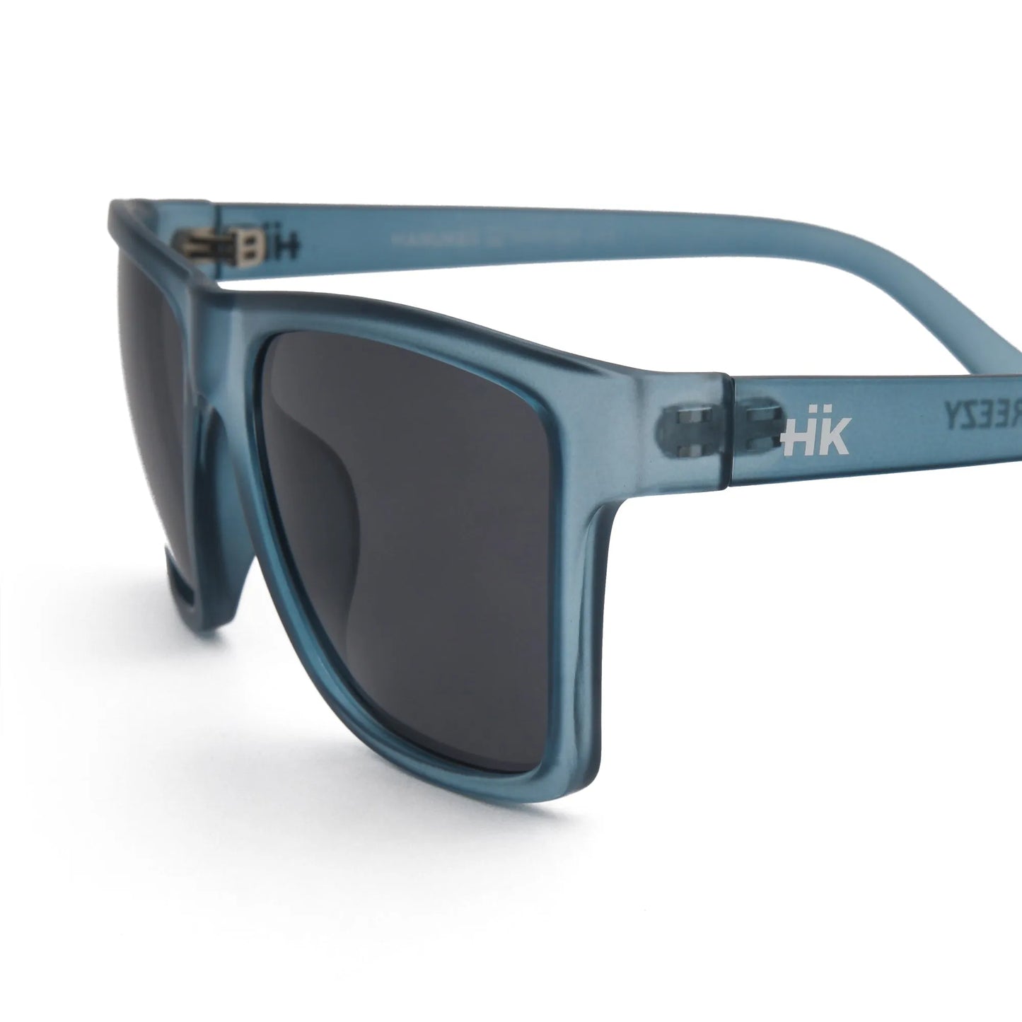 Nahaufnahme der Sonnenbrille Breezy Blue Hanukeii von INDICOM BRANDS SL, mit blauem Rahmen, dunklen Polycarbonat-Gläsern und weißem HK-Logo in der Nähe des Scharniers. Abgebildet auf einem sauberen weißen Hintergrund. UV400 Schutz sorgt für optimalen Augenschutz.