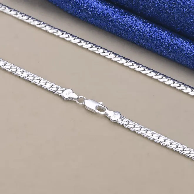 Eine Nahaufnahme der flyliving Halskette „Horst-Peter“ aus 925er Sterlingsilber mit Karabinerverschluss, dargestellt auf einer beigen Oberfläche mit blauem strukturiertem Hintergrund.