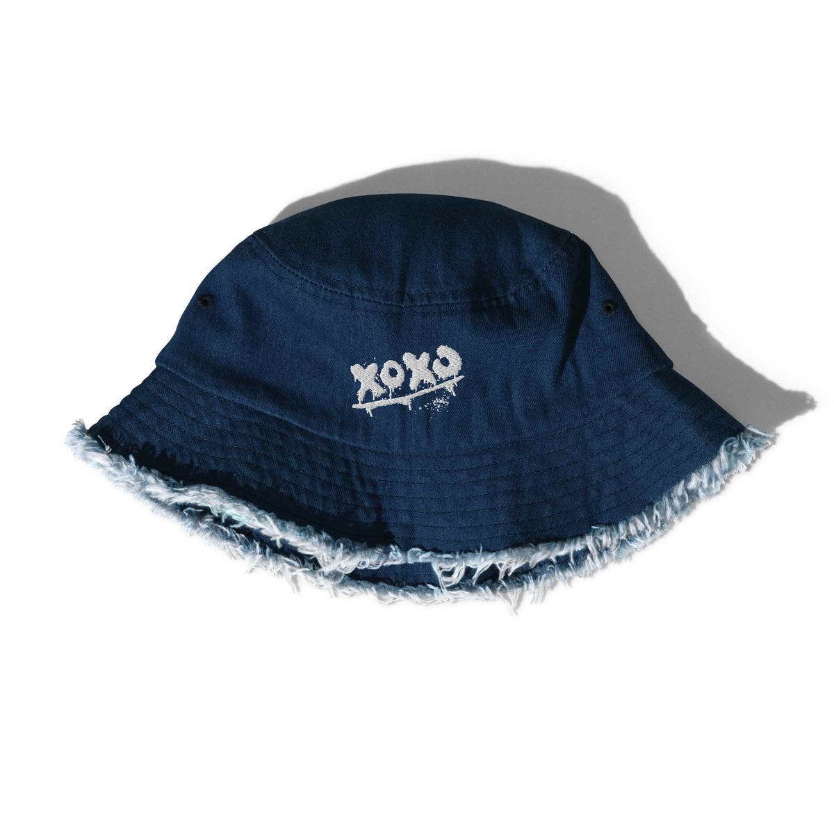 Fischerhut in Classic Denim mit „XOXO“-Stickerei und ausgefranstem Rand, schräg liegend mit Schatten