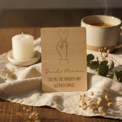 Eine hellfarbene holzkarte mit engraving hand hält herz und text danke mama für all die großen und kleinen dinge