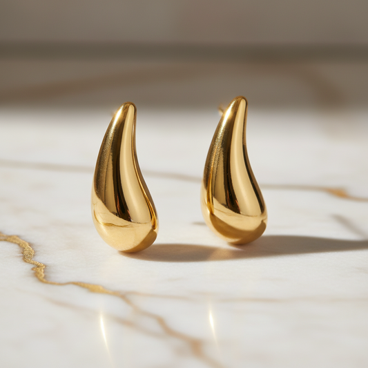 18K gold-plated teardrop stud earrings by flyliving glistening on white marble with golden veins.