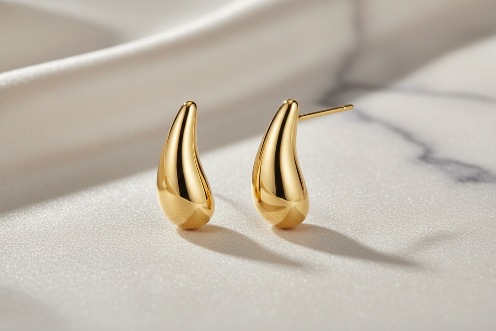 Golden Teardrop 18K gold-plated stud earrings by flyliving, with smooth polished tops and textured bottoms on white fabric.