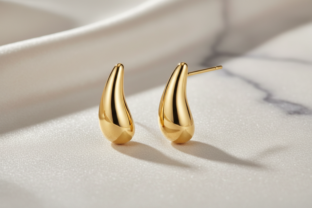 Golden Teardrop 18K gold-plated stud earrings by flyliving, with smooth polished tops and textured bottoms on white fabric.