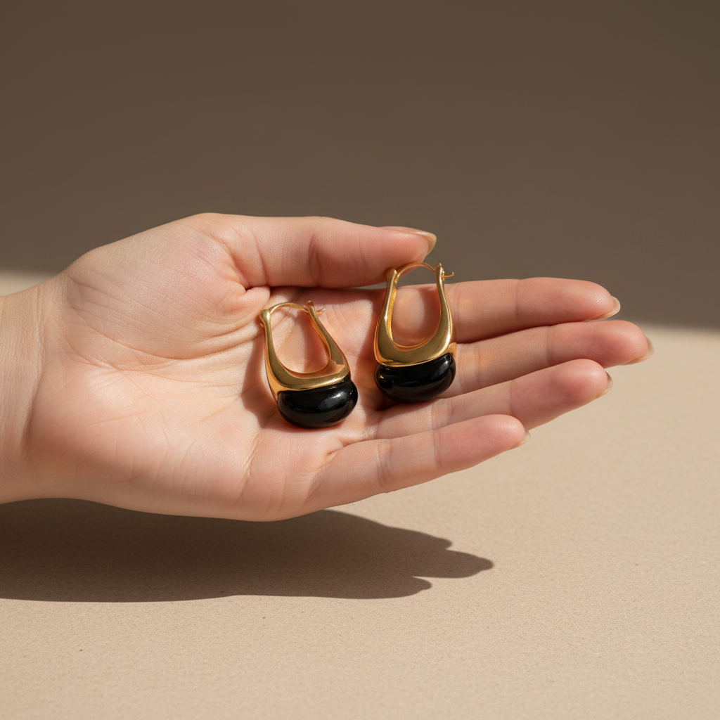 Gold and black onyx drop earrings by flyliving, held in an open hand.
