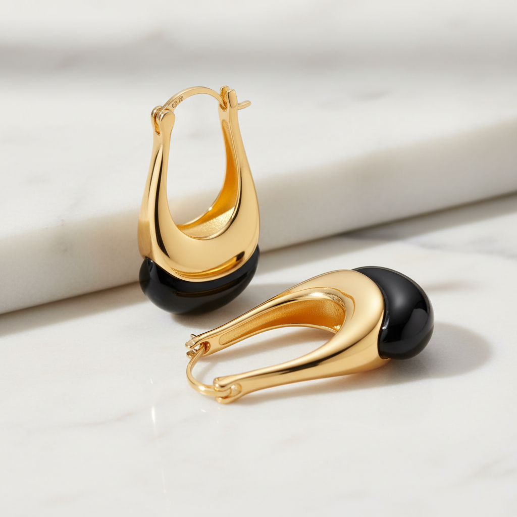 Gold-plated sterling silver and black agate drop earrings by flyliving, featuring a two-tone curved design on a marble surface.