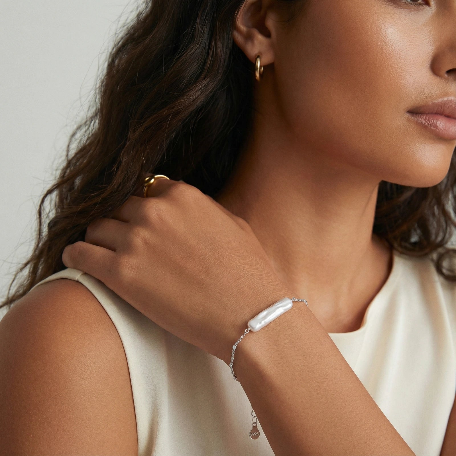 Barockperlenarmband von flyliving, silberfarbenes Kettchen, getragen am Handgelenk, mit goldenem Ring und Ohrringen.