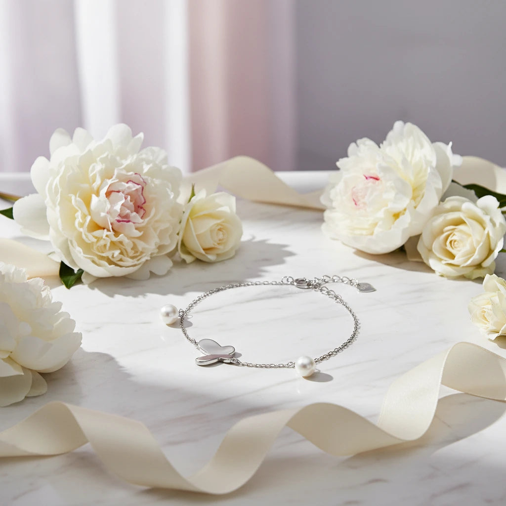 Silbernes Butterfly Dreams Armband von flyliving mit Perlen und schimmerndem Schmetterling, auf Marmor neben Blumen und Band.
