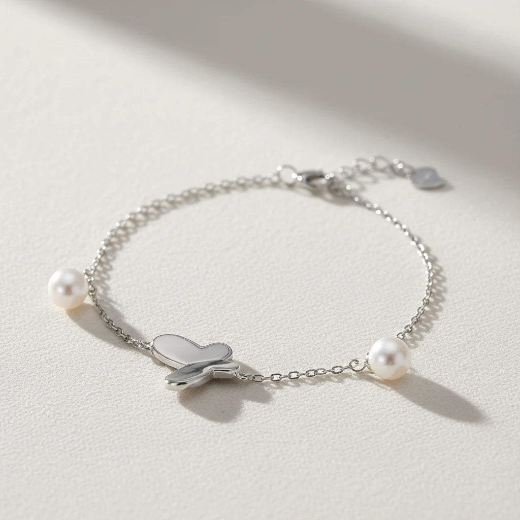 Silbernes Armband mit Schmetterling und Perlen von flyliving, filigrane Kette auf hellem Untergrund.