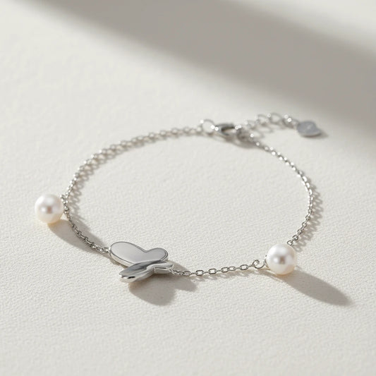Silbernes Armband mit Schmetterling und Perlen von flyliving, filigrane Kette auf hellem Untergrund.
