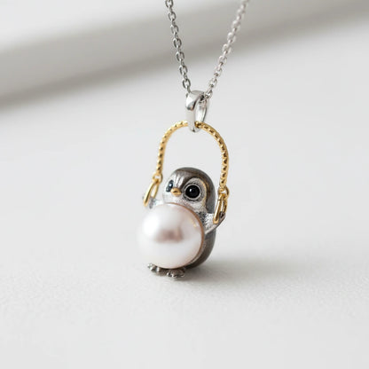 Perlenhalskette "Weise Eule" von flyliving, mit Anhänger eines Pinguins, der eine Perle hält und an einem goldenen Bügel hängt.