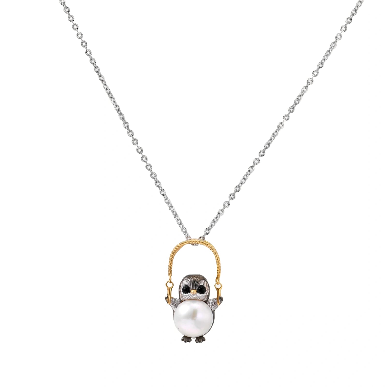Whimsical owl pendant holding a white pearl on a gold swing, rhodium-plated silver chain on cream background.