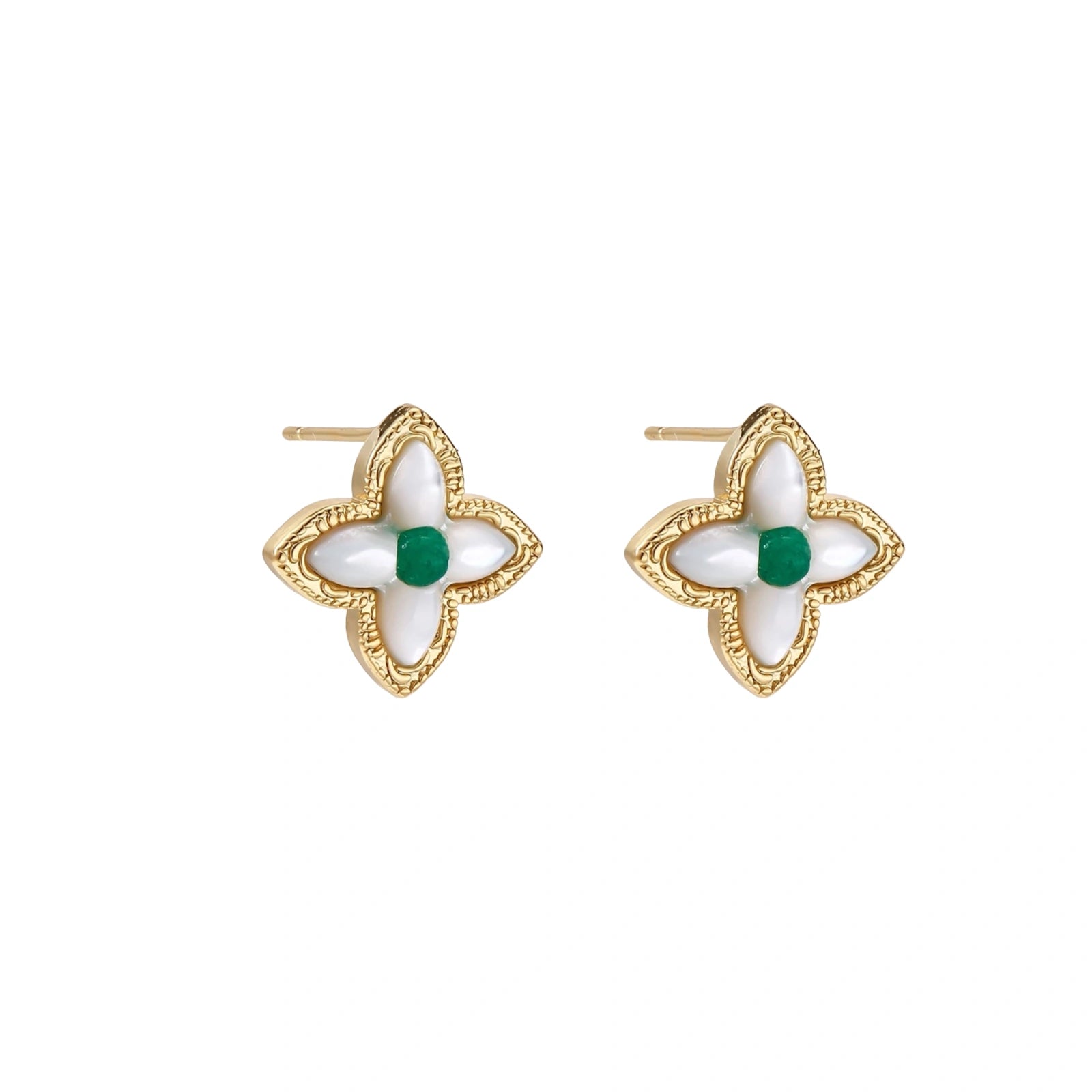 Gold quatrefoil stud earrings with white mother-of-pearl petals and emerald green gemstone center on beige background.