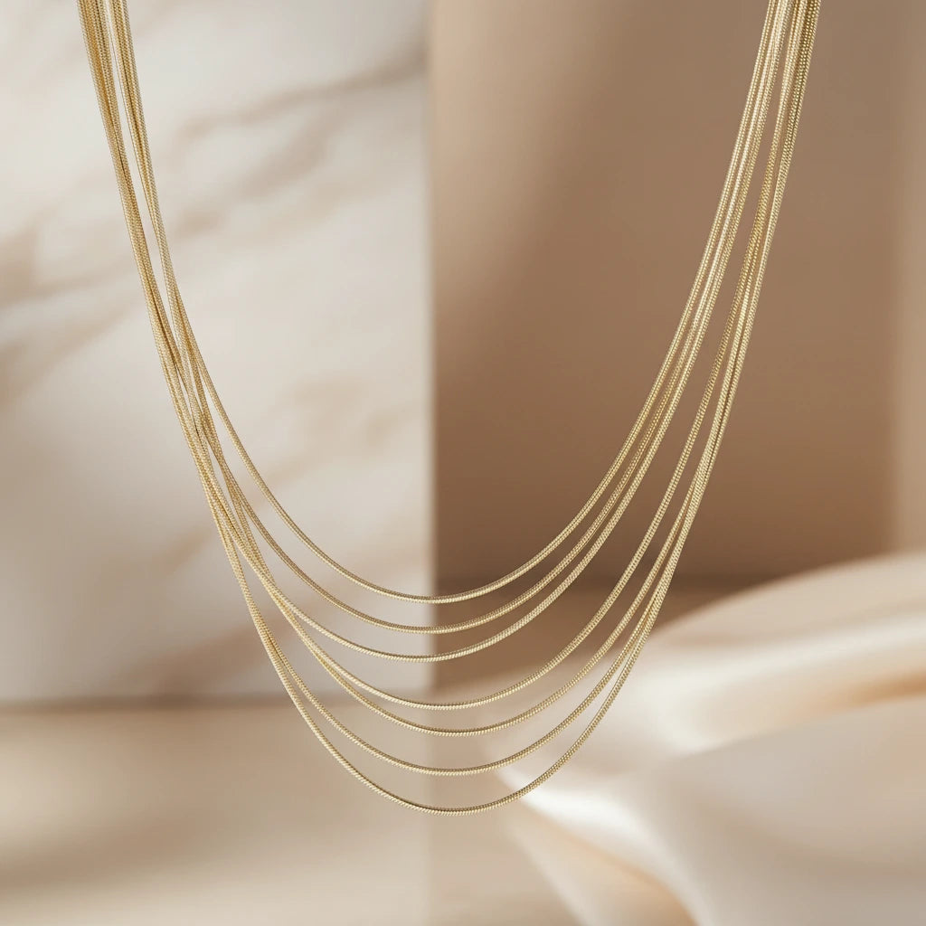 Mehrreihige goldfarbene Halskette von flyliving, filigrane Schlangenkettchen in unterschiedlichen Längen vor hellem Hintergrund.
