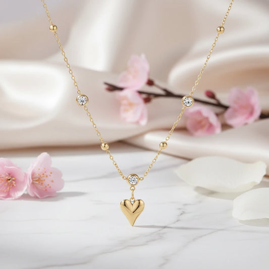 Goldene Kristallherz-Charm-Halskette von flyliving, mit Zirkonia besetzt, vor blumigem Hintergrund.
