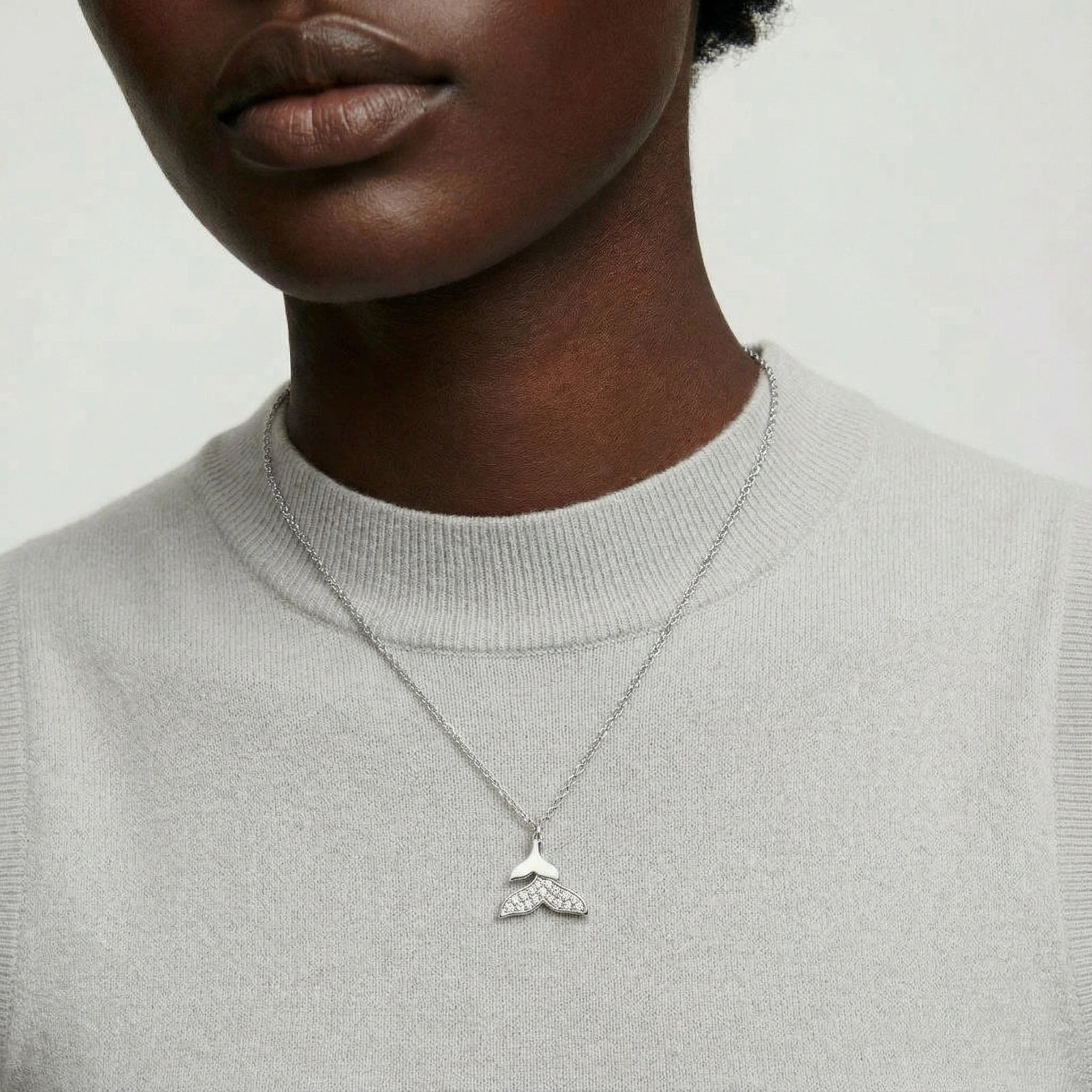 Kristall-Halskette mit Walflosse von flyliving, mit silberner Kette und hellem Pullover.