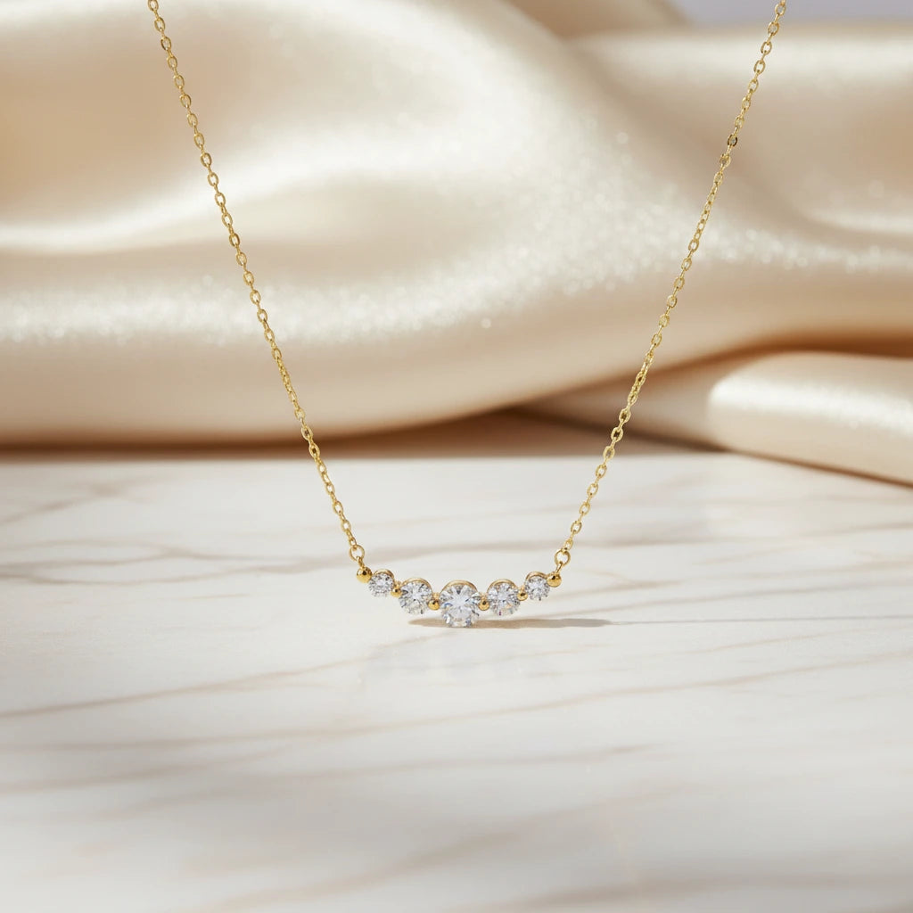 Vergoldete Golden Arc Halskette von flyliving, mit fünf Zirkonia Steinen auf Marmor und Seide drapiert.