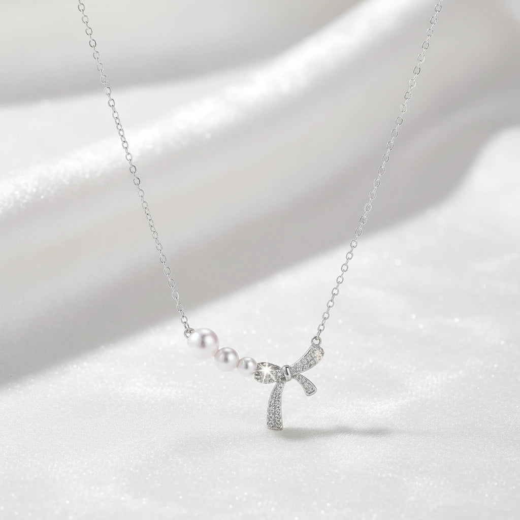 Versilberte Perlen-Schleifenhalskette von flyliving, mit drei Perlen und Schleifenanhänger auf einem weißen Hintergrund.