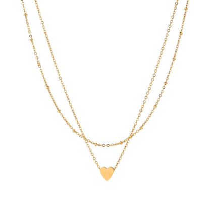 Delicate double-chain gold necklace with tiny heart pendant on cream background