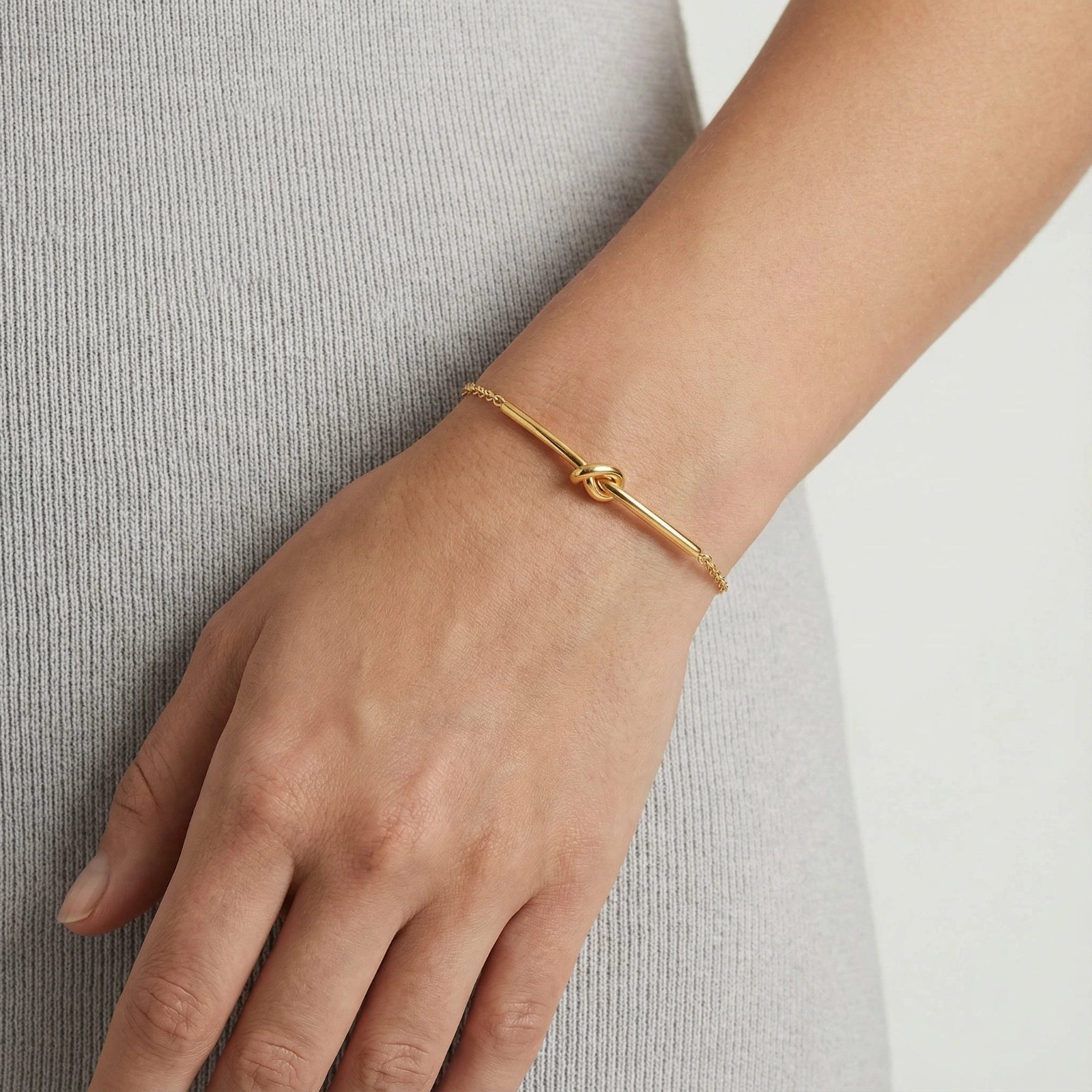 Goldenes Twisted Knot Bar Armband von flyliving, getragen am Handgelenk einer Person.