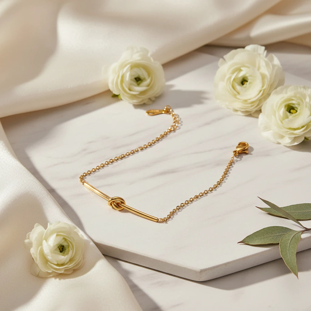 Goldenes Twisted Knot Bar Armband von flyliving, auf Marmor mit weißen Ranunkeln und grünen Blättern drapiert.
