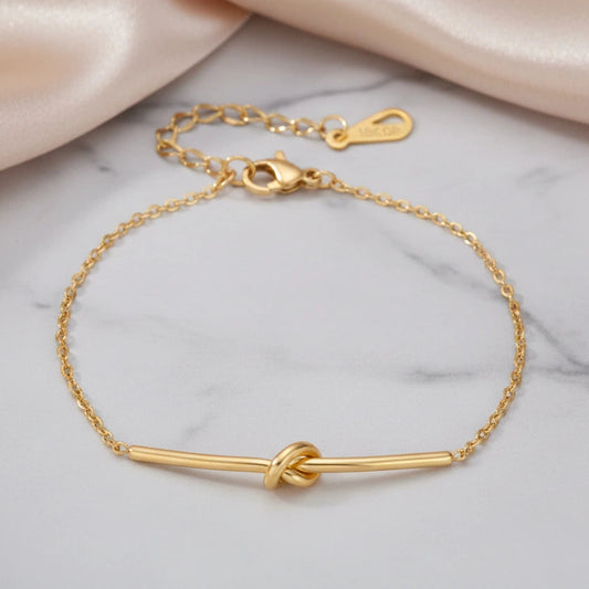 Goldenes Twisted Knot Bar Armband von flyliving, mit einem Knoten als Blickfang, auf Marmor Hintergrund.