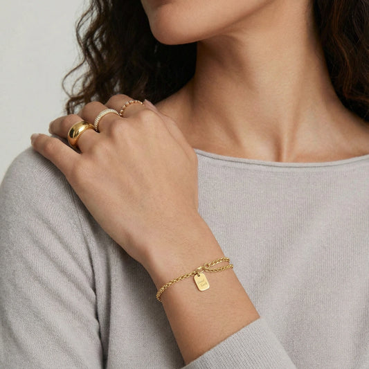 Vergoldetes Good Luck Armband von flyliving, mit einem kleinen Anhänger, getragen am Handgelenk mit Ringen an der Hand.