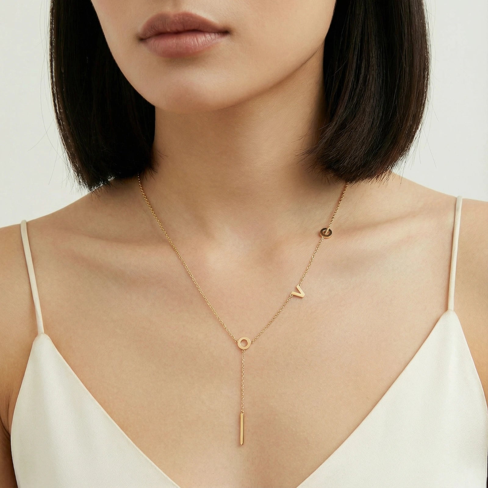 18K gold-plated LOVE Y-chain necklace by flyliving, featuring individual letters and a bar pendant, worn on a woman's neck.