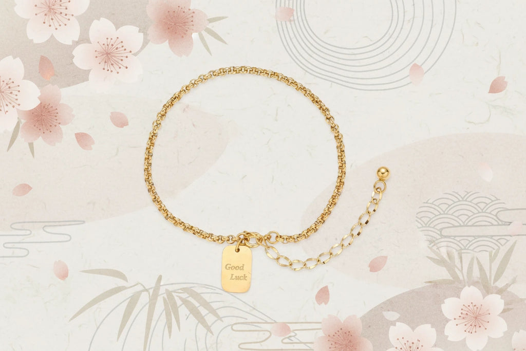 Vergoldetes "Good Luck" Armband von flyliving mit dekorativen Kirschblüten und Wellenmuster auf beigem Grund.