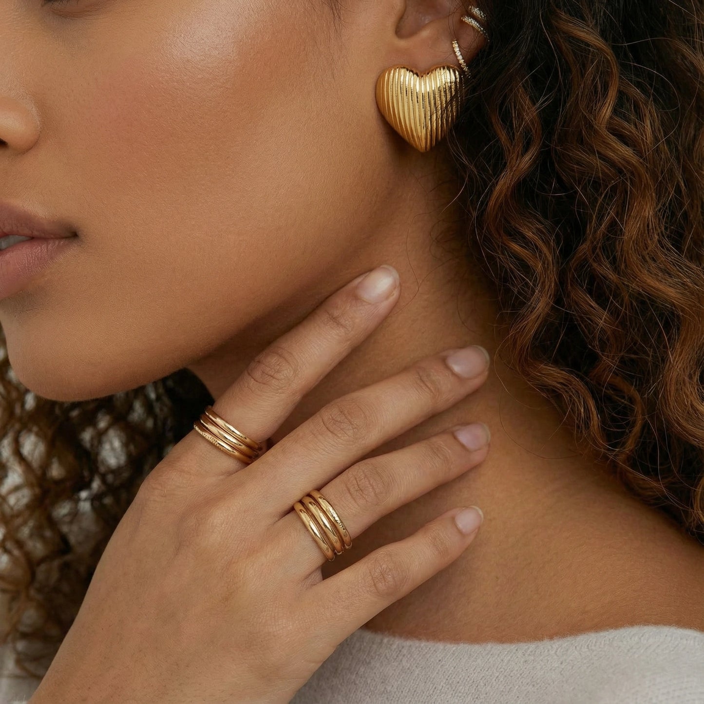 18K gold-plated ridged heart stud earrings by flyliving, worn by a model with other ear cuffs and gold rings.