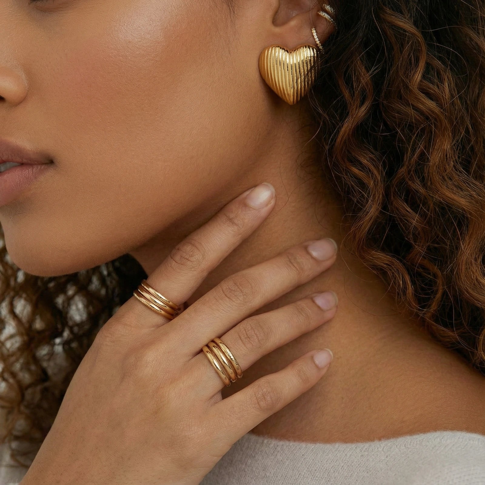 18K gold-plated ridged heart stud earrings by flyliving, worn by a model with other ear cuffs and gold rings.