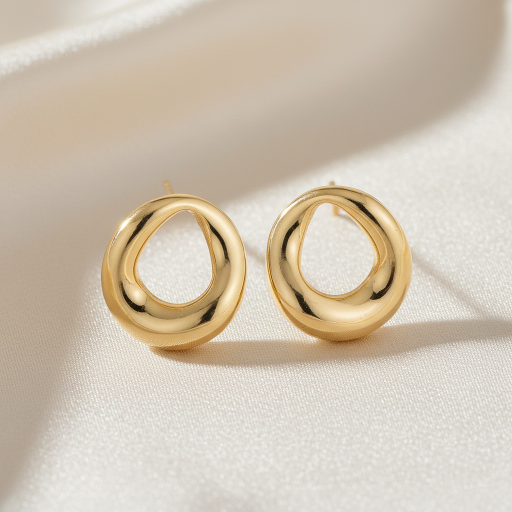 Golden stud earrings by flyliving, featuring an abstract, organic loop design on white fabric.