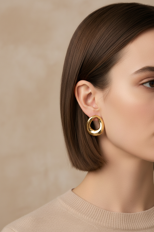 Golden large irregular hoop earring by flyliving, worn on a woman's ear with a beige ribbed sweater.