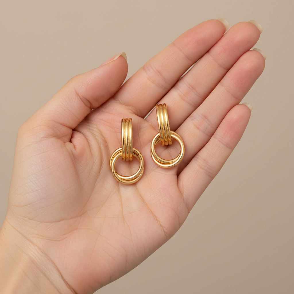 Geometric 18K gold-plated stainless steel statement earrings by flyliving, featuring linear loop drops, held in an open hand.