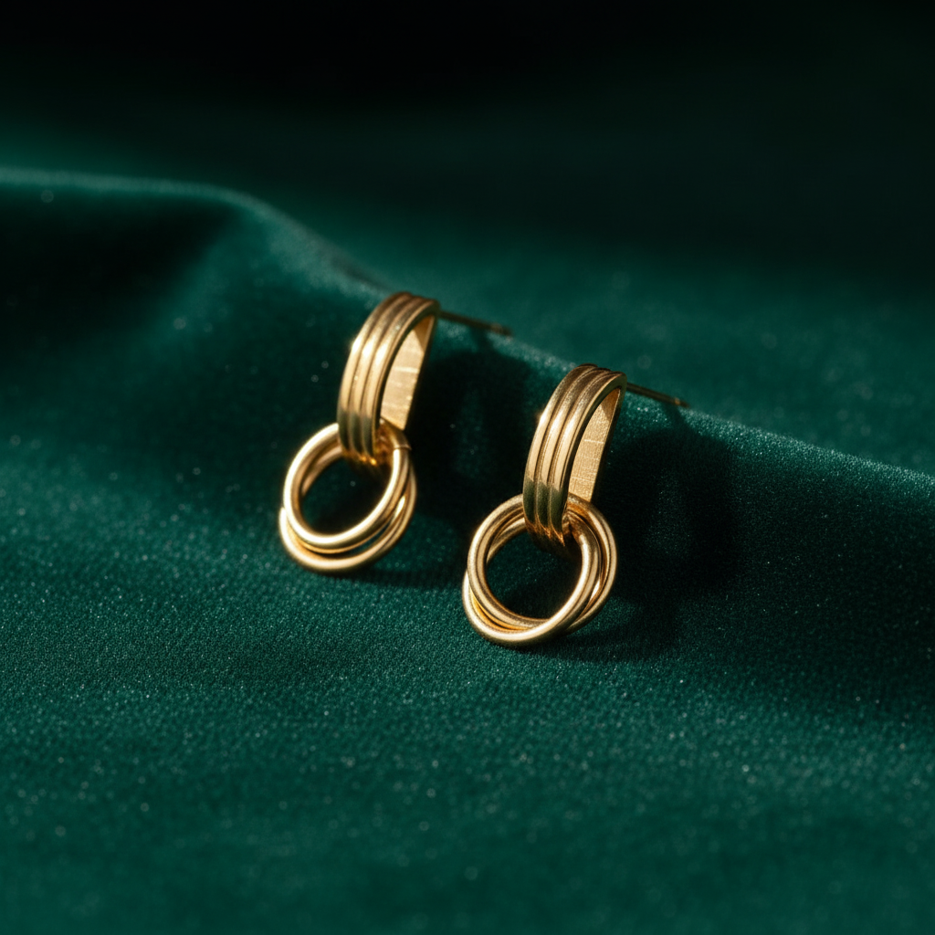Gold geometric linear loop drop earrings by flyliving, featuring ribbed studs and interlocking rings on green velvet.