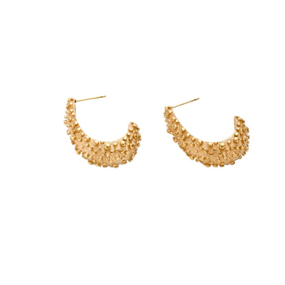 Curved gold hoop earrings with raised granulated texture resembling sea urchin surface on cream background