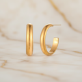 Gold-plated stainless steel hoop earrings by flyliving, displayed as a pair on a marbled surface.