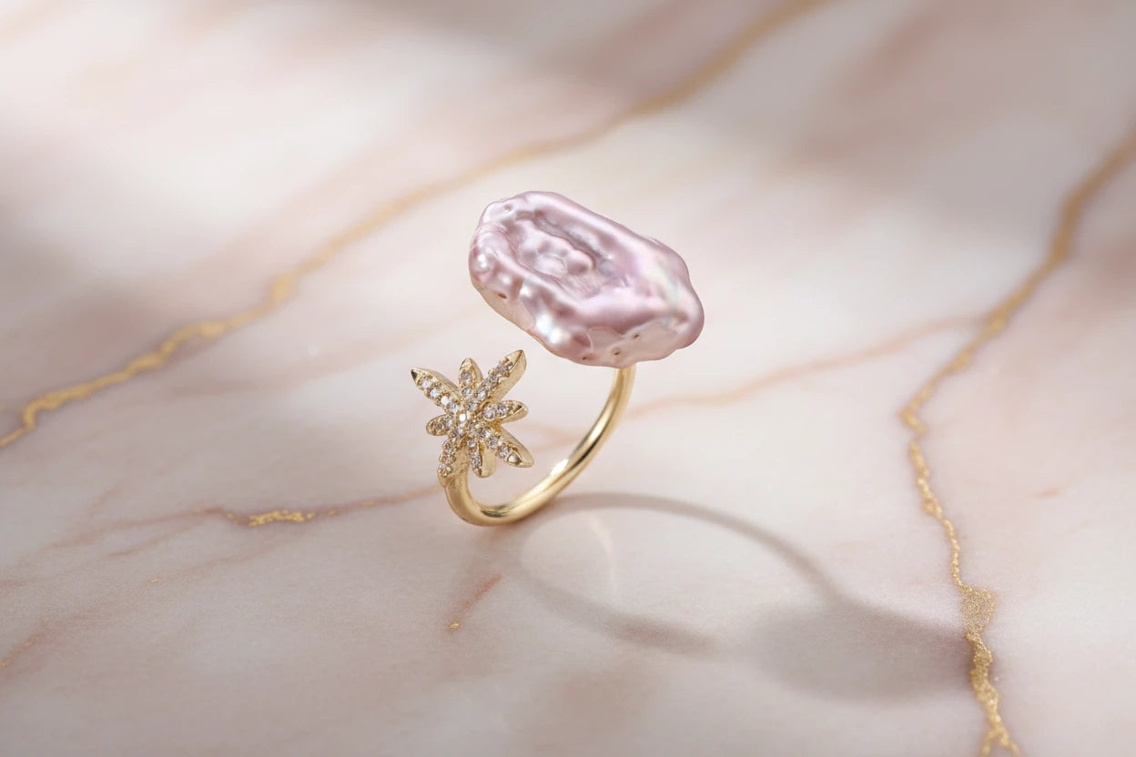 Perlenring mit Sternenstaub-Akzent von flyliving, auf einem marmorierten Untergrund mit goldenen Adern liegend.