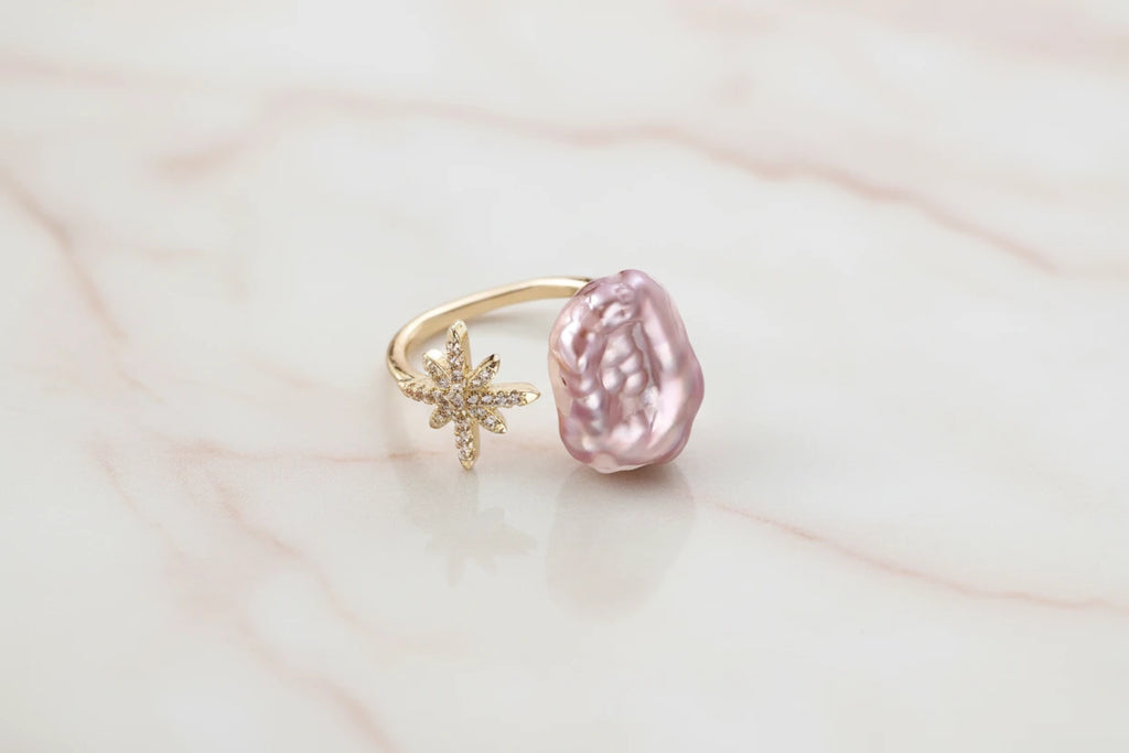 Goldener Sternenstaub-Perlenring von flyliving mit einem großen, rosa Barockperlen-Akzent.